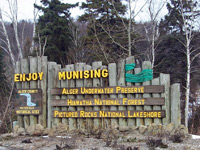 This entrance sign at the City of Munising's boundaries includes a waterfall sketch and rope coil on a vertical log background.