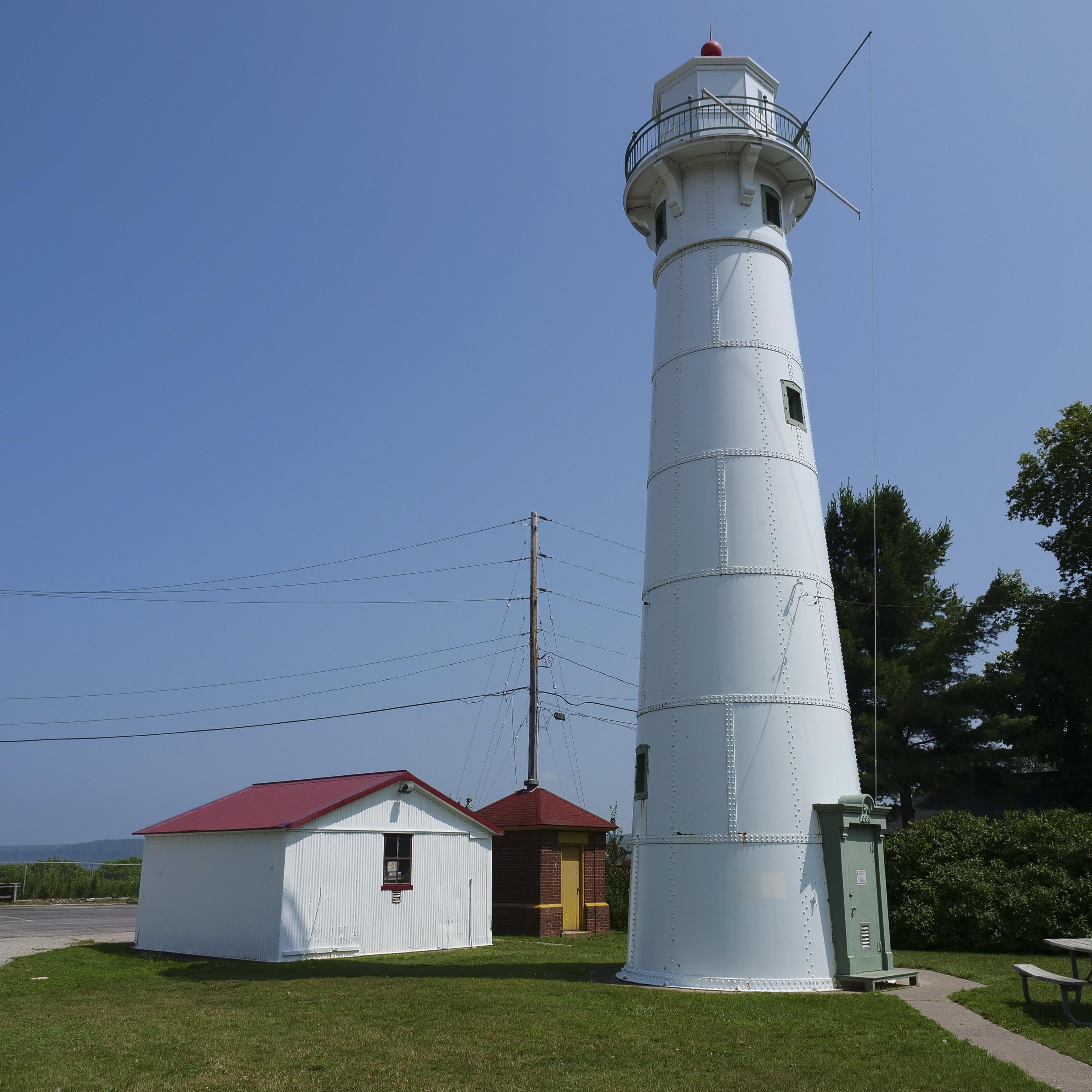 Munising Front Range Light A tall white lighouse with a green door and red top next to a white shed and brick support building