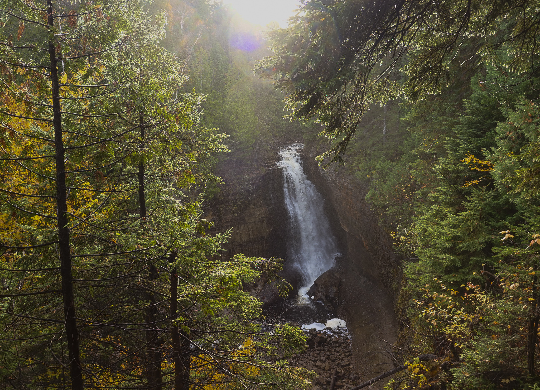 Miners Falls 2023 A large, powerful waterfall plunges off a sandstone cliff, surrounded by yellow and green foliage