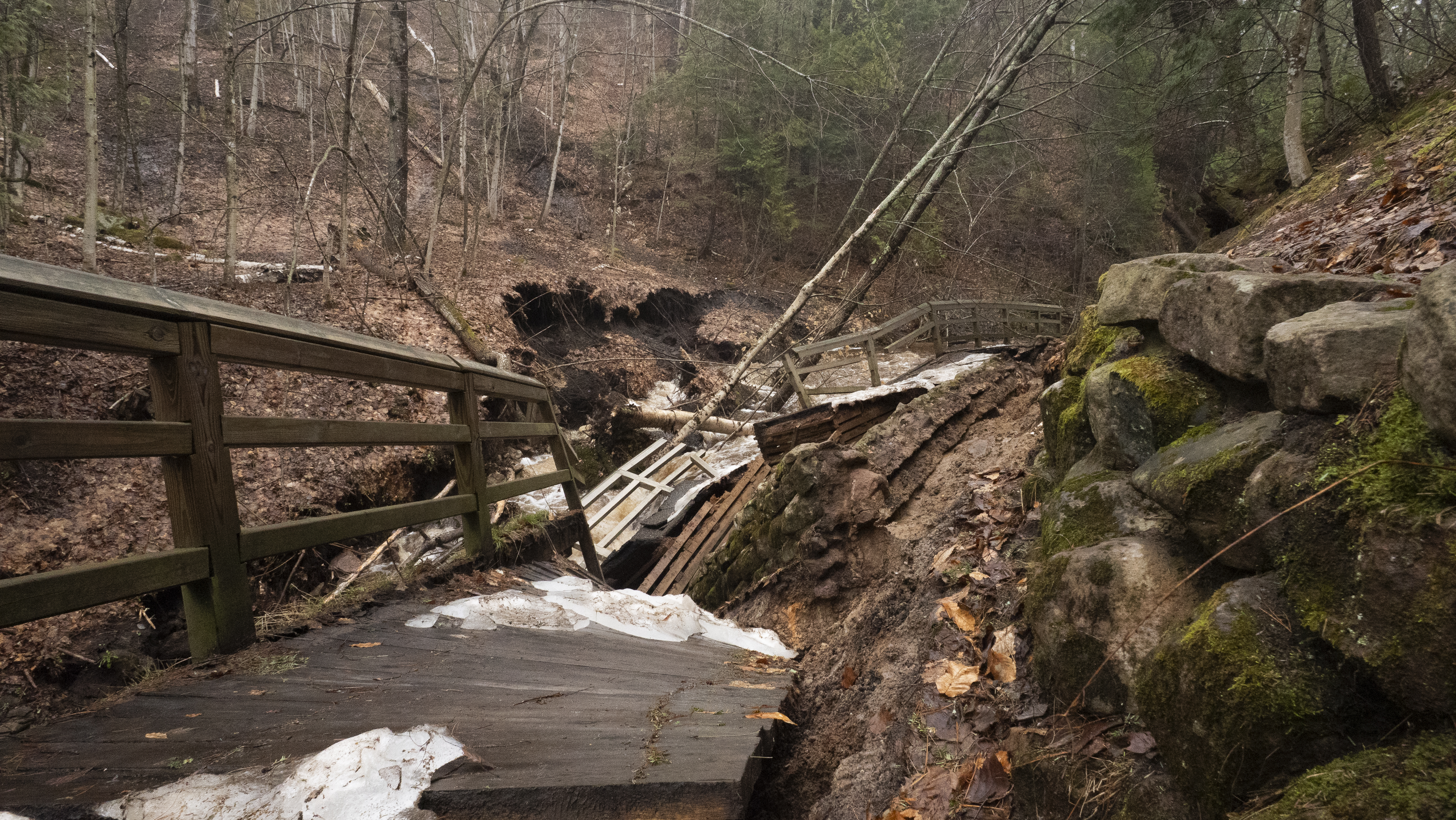 Damage on the Munising Falls Trail A badly damaged, paved trail falling into the river next to it.