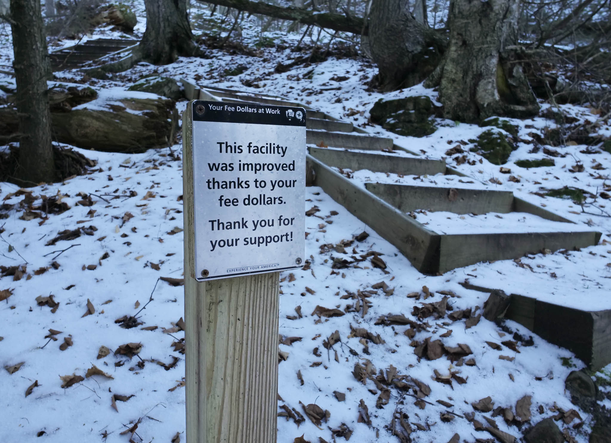 A sign in front of wood stairs reads "this facility was improved thanks to your fee dollars. Thank you for your support!"