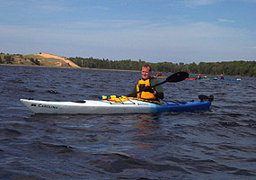 Visitor and kayak on the clear blue waters of Grand Sable Lake, with the Grand Sable Dunes towering in the distance.
