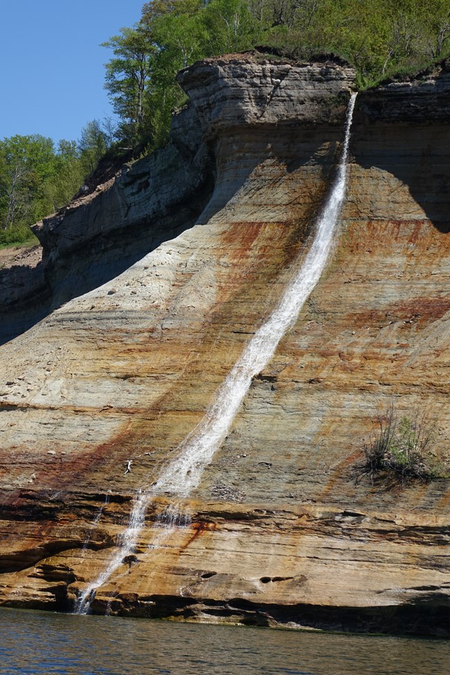 Water drops from the cliff top onto a sloping sandstone cliff and flows into Lake Superior