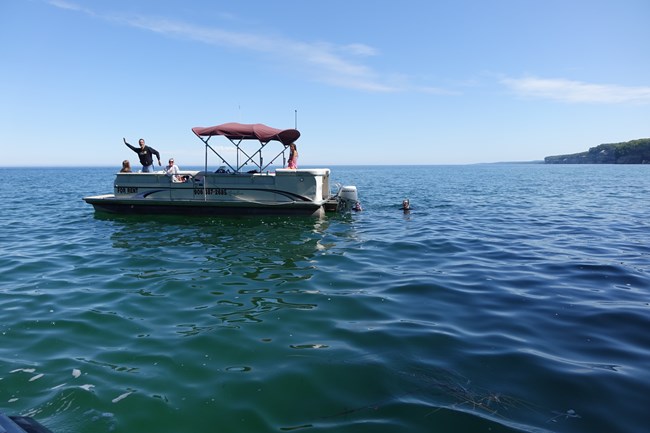 People on a pontoon boat and one person in the water on Lake Superior
