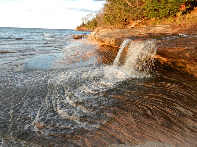 Small waterfall flows over rocky ledge into Lake Superior