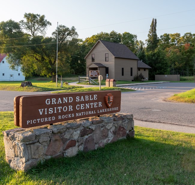 Wood and stone visitor center sign with two-story wood visitor center building in the background