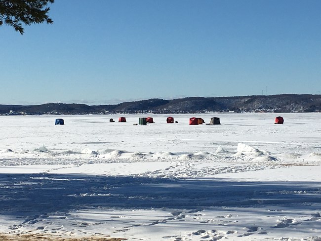 Ice fishing tent structures out on snow covered Lake Superior by Sand Point
