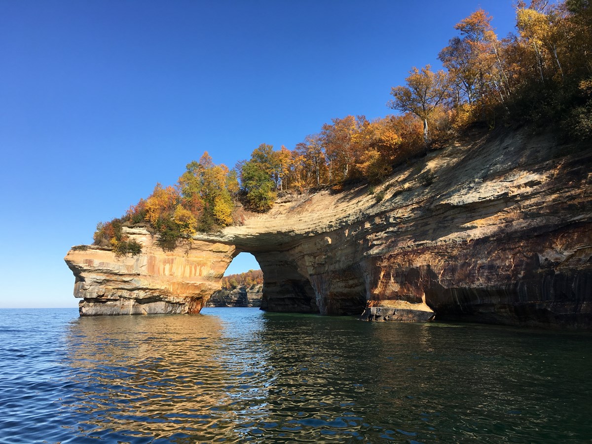 Rock archway sticking out into Lake Superior. Trees on top with leaves changing colors.