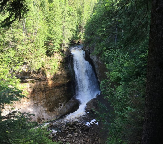 Miners waterfall flows out of the forest and crashes on the rocks below.