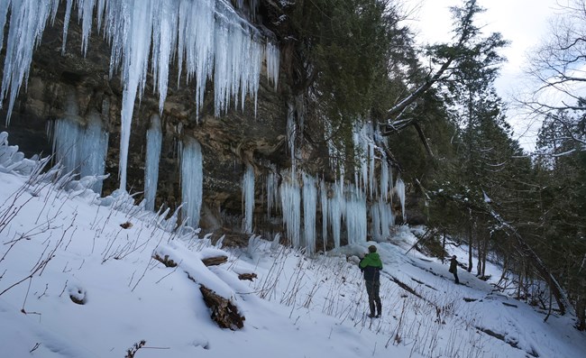 A person stands in front of gigantic blue ice formations