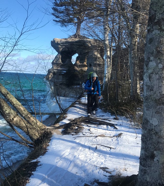 Backpacker walking on snow along lake shore