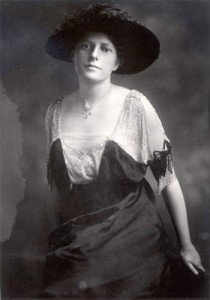A black and white photograph of a white woman in a formal dress and wide brimmed hat