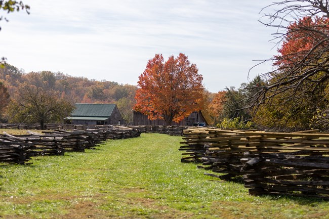 A grassy field with a wood fence and a couple wood buildings.