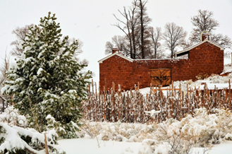 A snow-covered red brick fort with a fence and trees in the foreground
