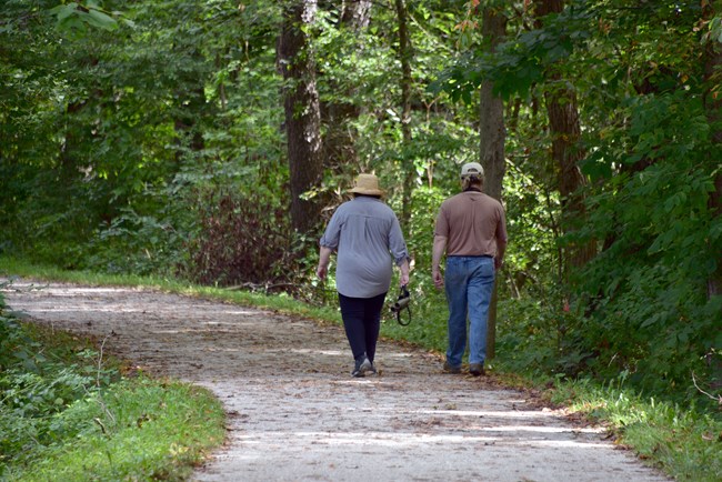 Two people walking along a gravel trail with trees surrounding them