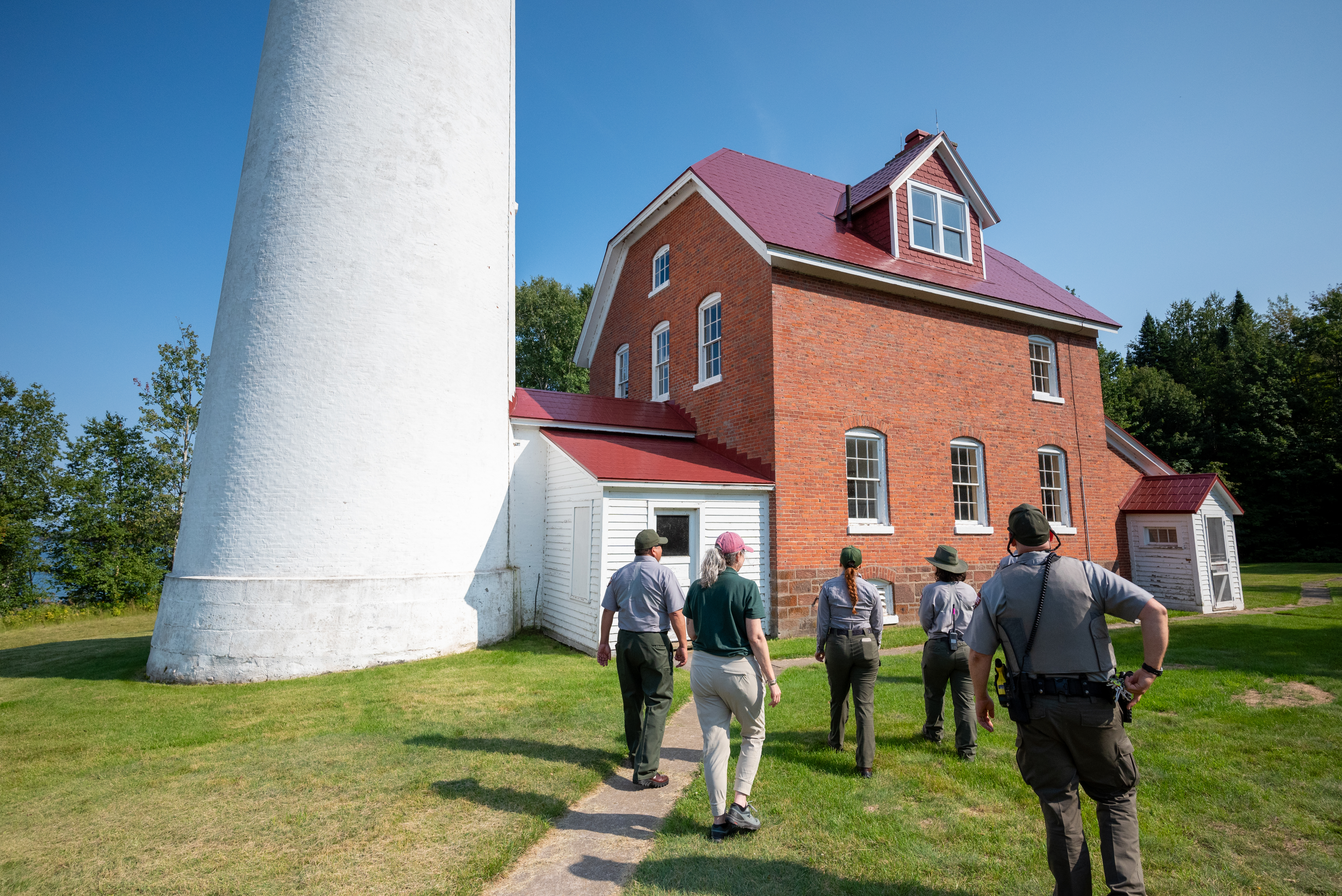 A group of people in National Park Service uniforms stand in front of a lighthouse as they walk along a path on a tour. A group of people in National Park Service uniforms stand in front of a lighthouse as they walk along a path on a tour.