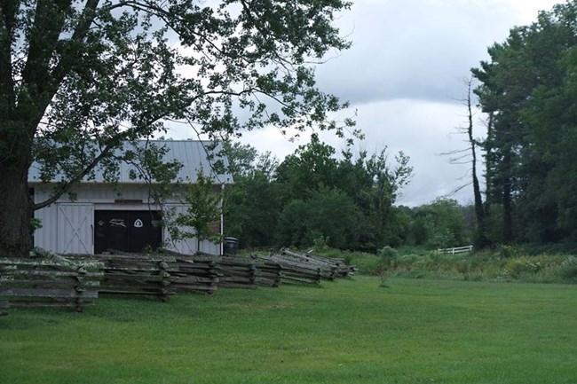 A white building stands behind a split rail fence and a green grass yard
