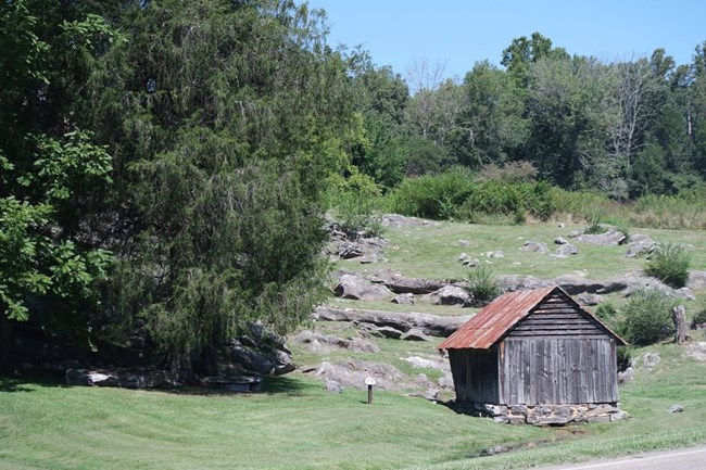 A spring house stands at the foot of a rocky hillside.