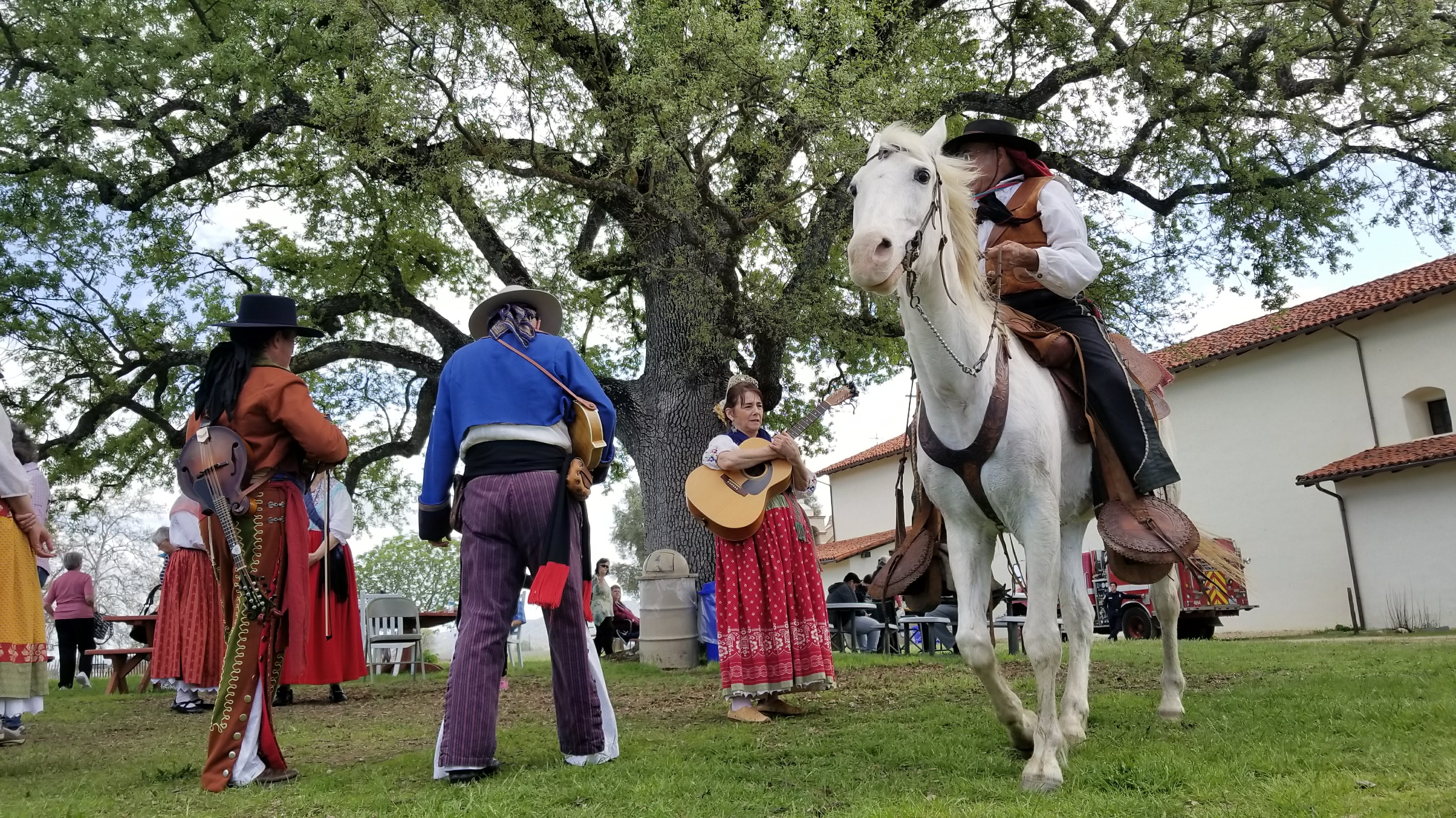 Mission Days San Antonio de Padua 2018 (86) Musicians playing music outside under a large oak tree with one musician on a horse.