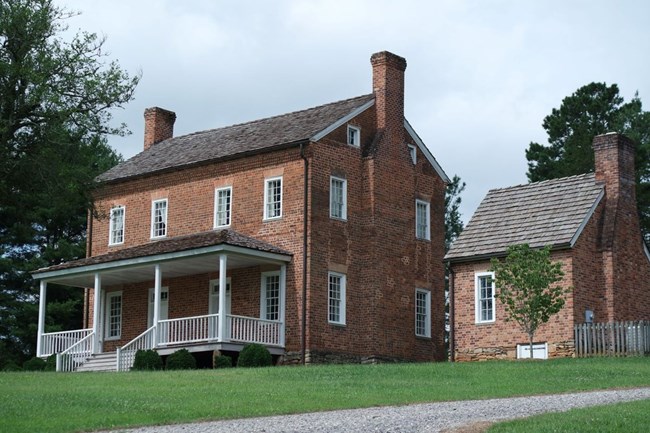 A two-story brick house with a large patio and several windows. There are trees surrounding it.