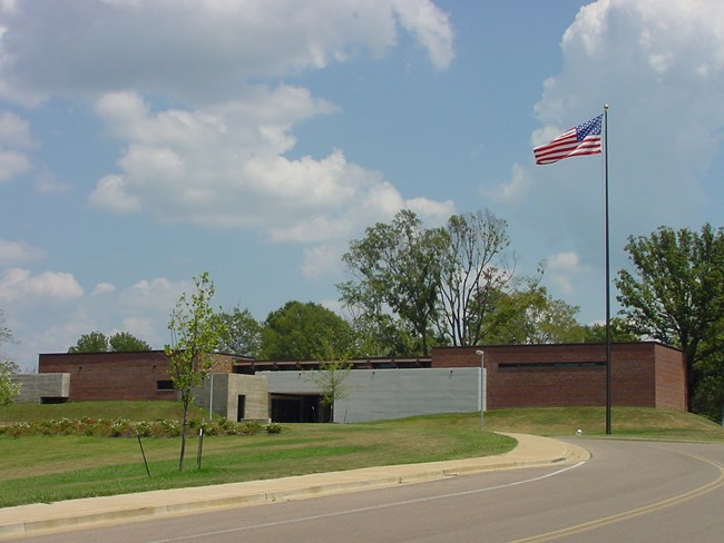 Brick building sitting on top of a grassy hill under a blue sky with white clouds.