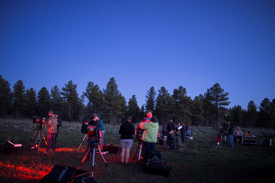 People setting up telescopes in a field at dusk People setting up telescopes in a field at dusk