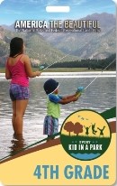 Two children fishing at a lake with mountains in the background.
