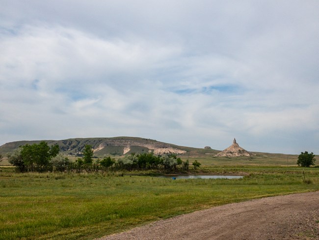 A chimney-shaped rock formation looms in the distance above a dirt road.