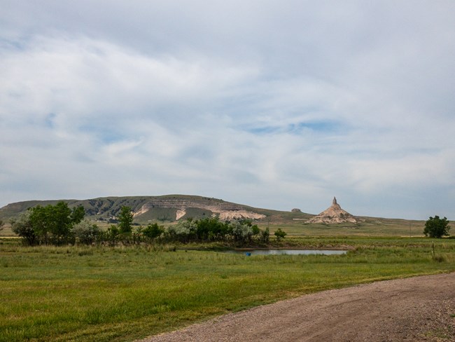 A chimney-shaped rock formation looms in the distance above a dirt road.