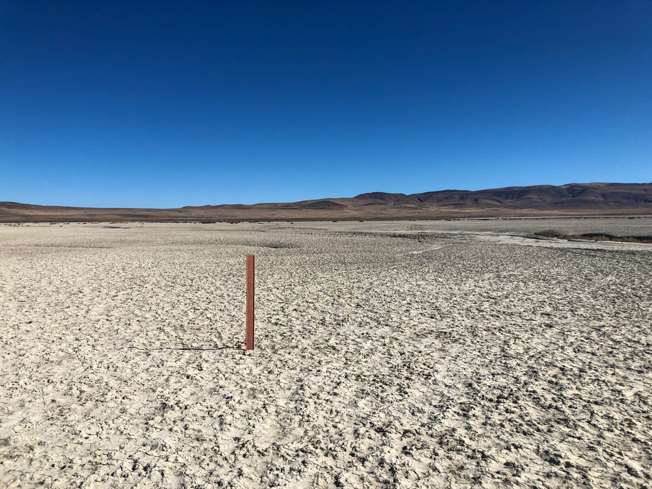 A trail marker stands in a large salt flat.