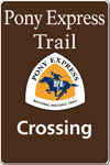 A brown tall rectangular highway sign with white text saying: Pony Express Trail Crossing and a triangular logo with orange and white and a blue pony rider. A brown tall rectangular highway sign with white text saying: Pony Express Trail Crossing and a triangular logo with orange and white and a blue pony rider.