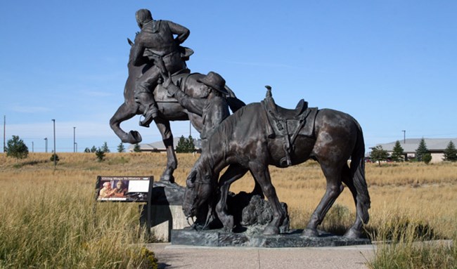 A single horse stands in front of a Pony Express rider on a horse in the form of a large bronze sculpture. An exhibit sits to the left.