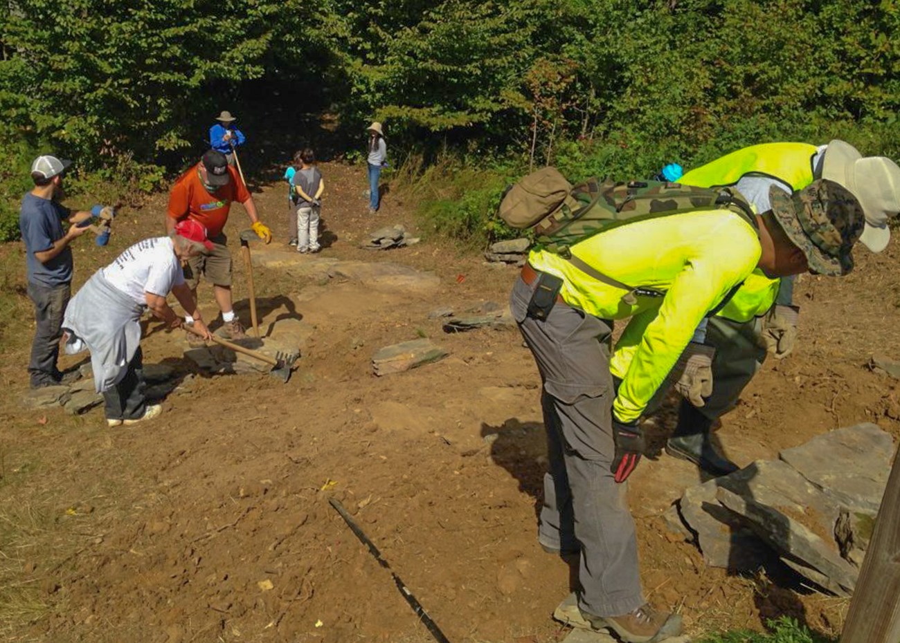 Volunteers work on installing stone steps on an earthen slope of the trail.