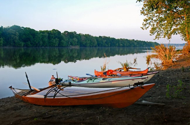 Kayaks resting on the shore of the Potomac River with the river and treeline in the background.