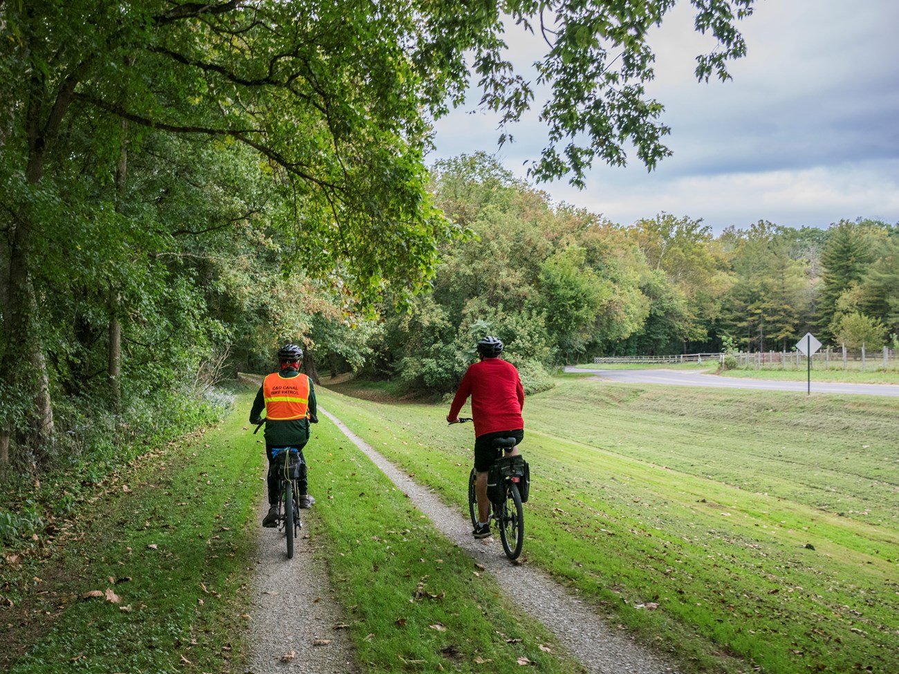 Two bikers travel along the grass and gravel towpath