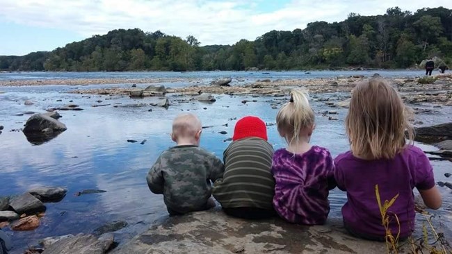 Children sitting on rocks near shore of waterway Children sitting on rocks near shore of waterway
