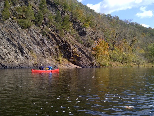 Canoeing Paw Paw Bends of the Potomac River two people in a canoe on a river with rock outcropping and steep hillside in the background