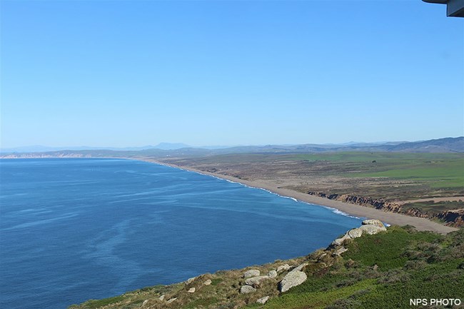 A long straight beach stretches off into the distance, separating the ocean on the left from the land on the right.