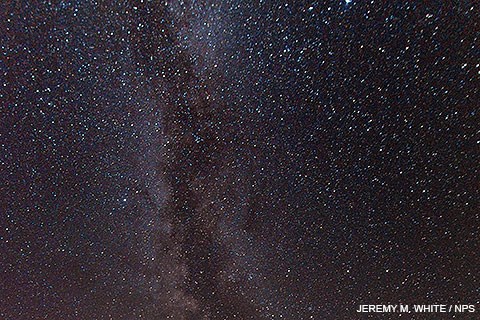 The Milky Way. Jeremy M. White / NPS. Hundreds of white dots against a black background with two thick irregularly-shaped white lines running vertically just left of center.
