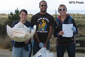 Three Beach Cleanup Volunteers holding litter collected from a beach.
