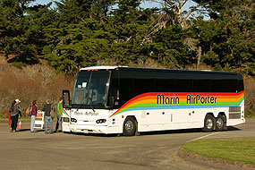 A white coach-sized bus painted with a rainbow-colored horizontal stripe below the windows on its sides.