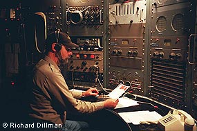 A bearded man wearing a ball cap sits at an old radio transmitting station.