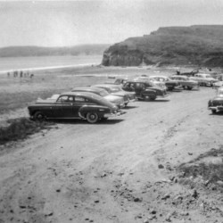 Black and white photo of cars in a parking lot adjacent to the beach.