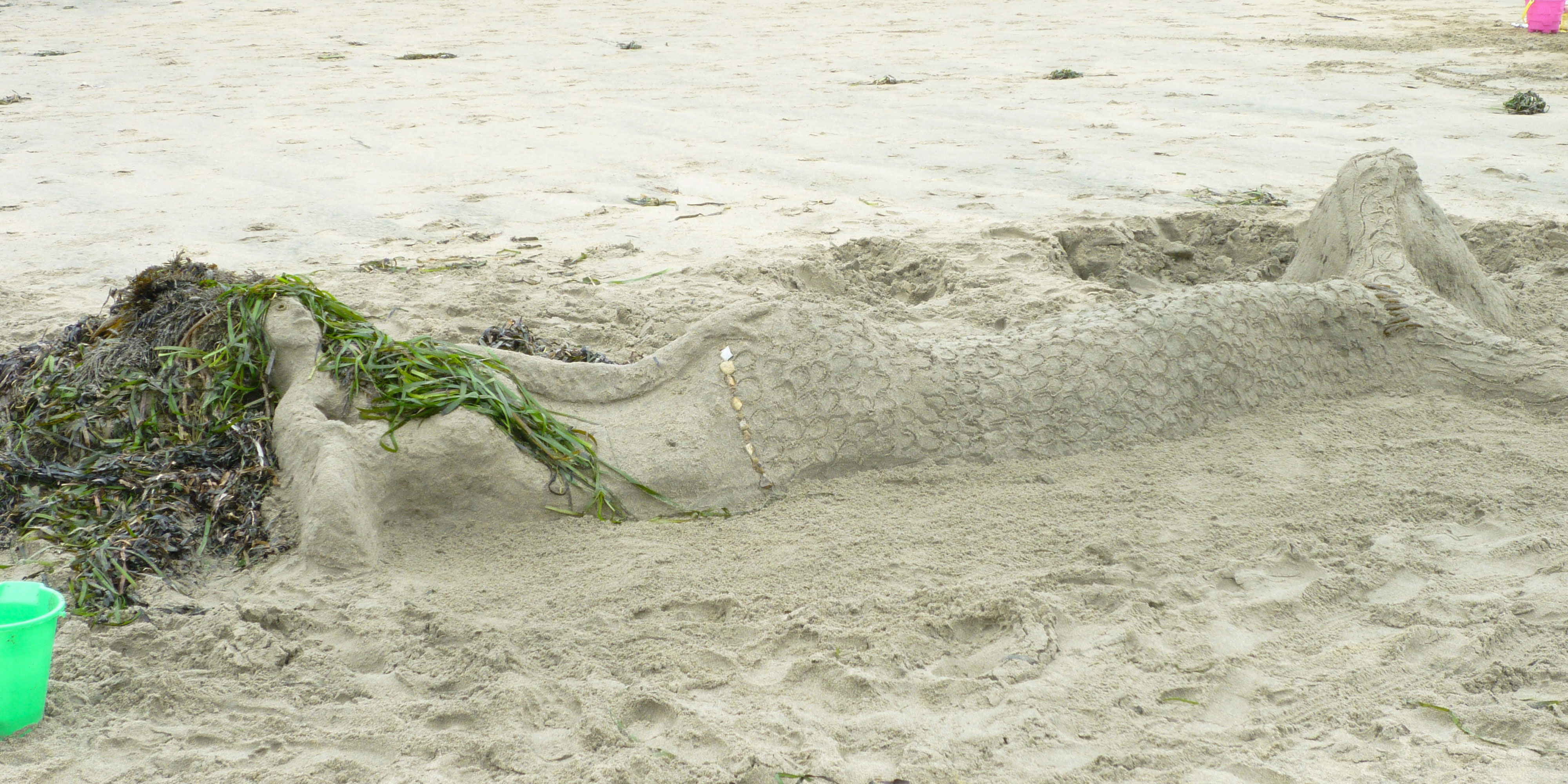 A sand sculpture of a mermaid with hair made of kelp.