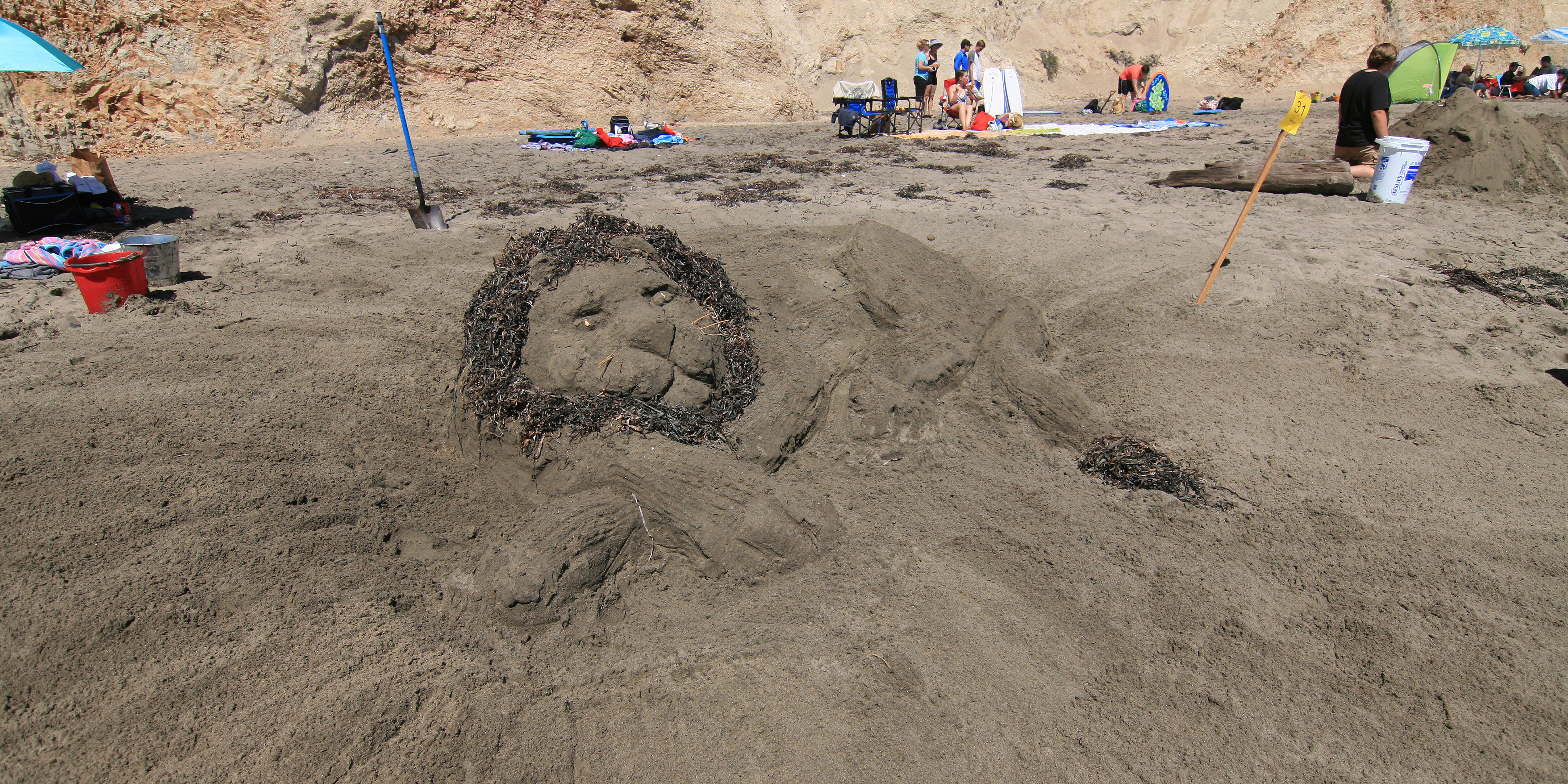 A large sand sculpture of lion with a mane made of seaweed.