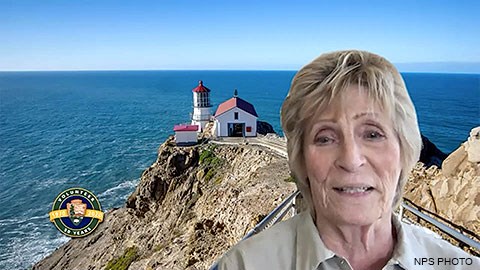 An elderly woman with short blond hair with an image of a lighthouse and the ocean in the background.