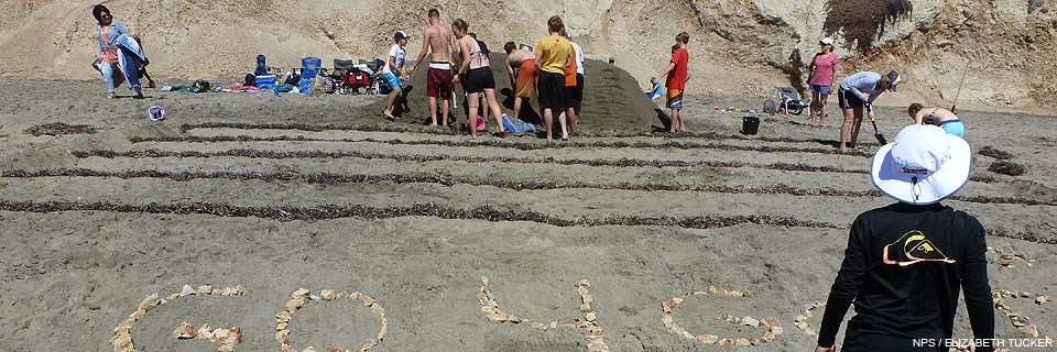 Young adults constructing a sand sculpture of bleachers and a foot-race track.