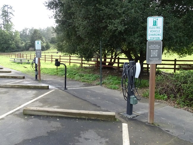 Two sets of Tesla charging stations on black posts adjacent to signs indicating "Pay per use. Electric vehicle charging only. Scan for Instructions to Charge a Non-Tesla."