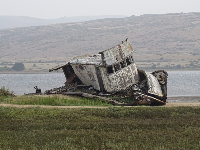 A derelict fishing boat on the edge of narrow bay with a grass-covered ridge in the background.
