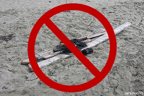 Long pieces of wood on a sandy beach which are burnt in the middle, overlaid by a red circle with a diagonal line.